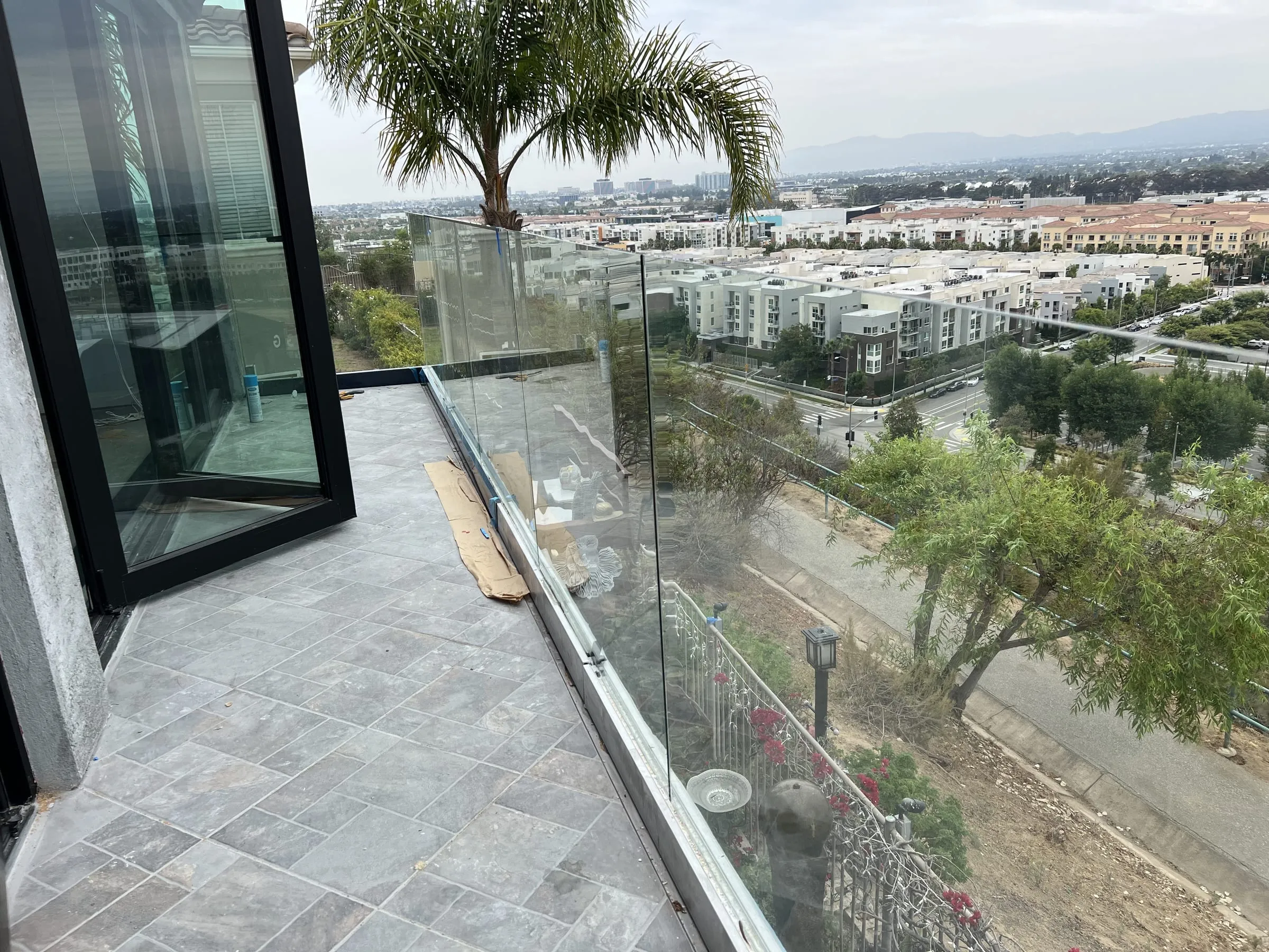 Frameless glass balcony railing outside a black-framed door, with a wide city view