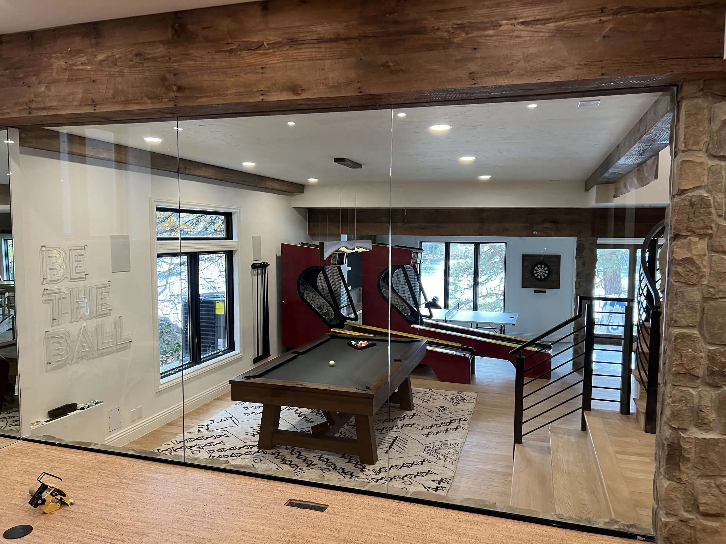 Frameless glass wall under a timber beam, looking into a billiards room