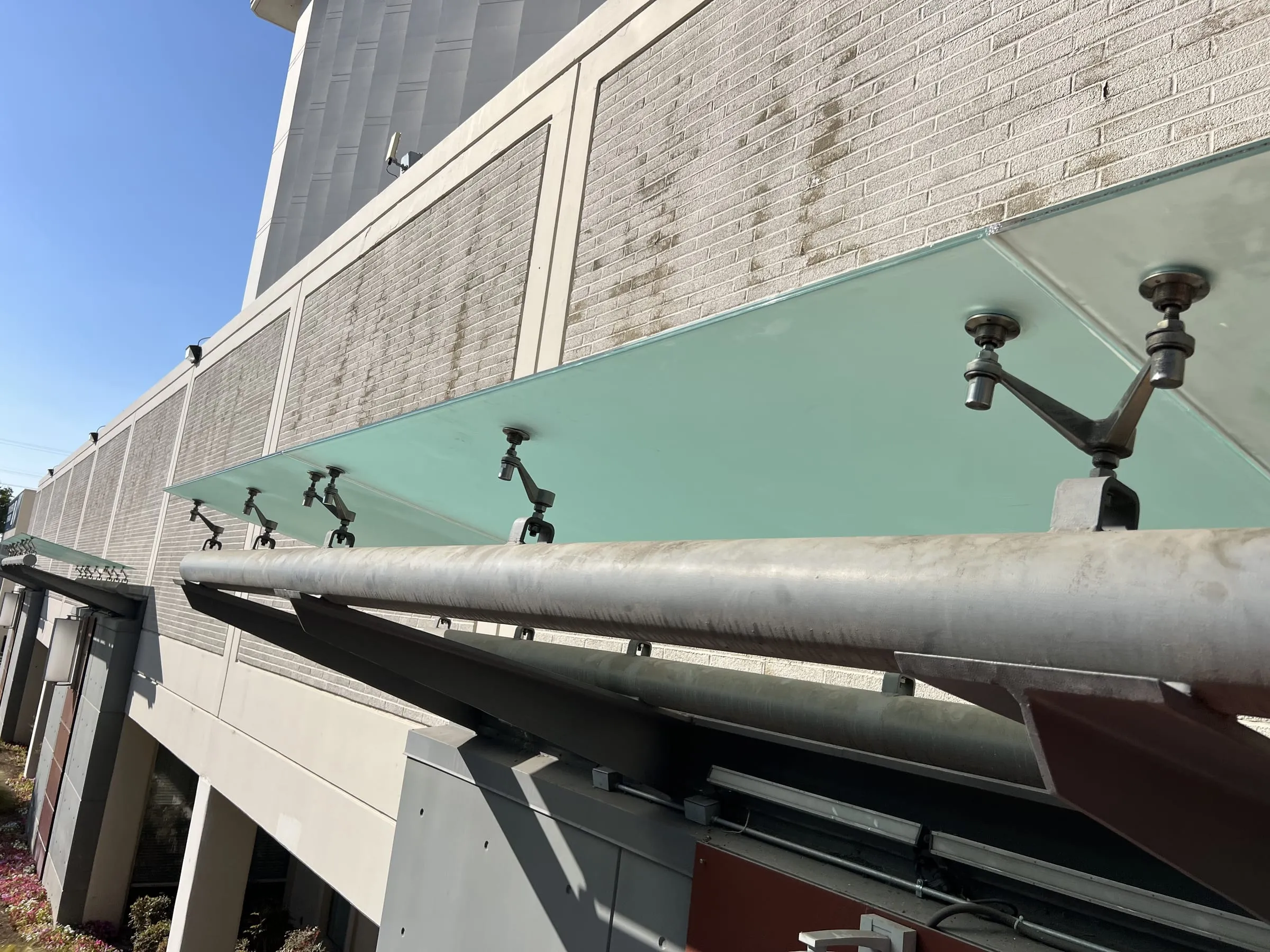 Frosted glass canopy on stainless spider fittings and steel outriggers along a building facade