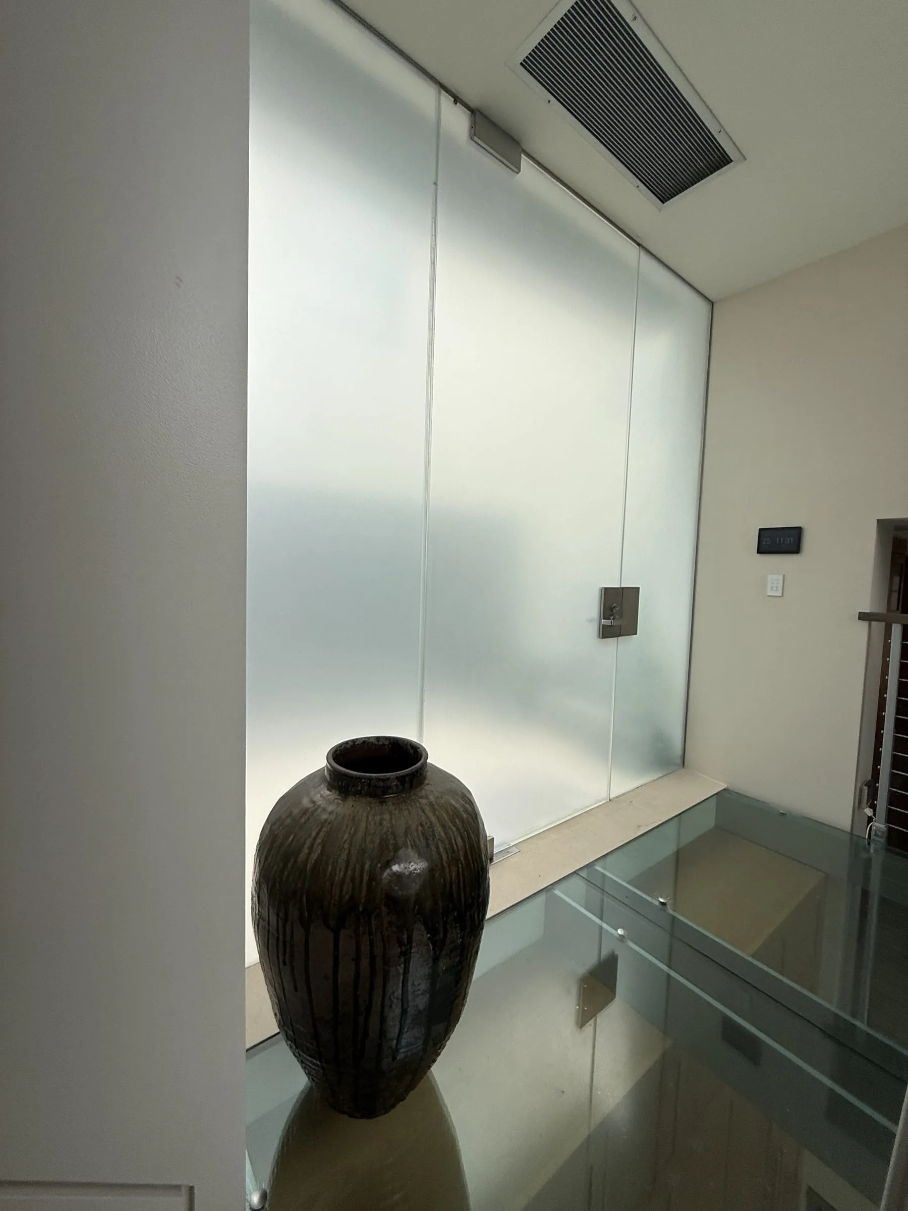 Frosted glass wall above a glass landing, with a dark vase in front