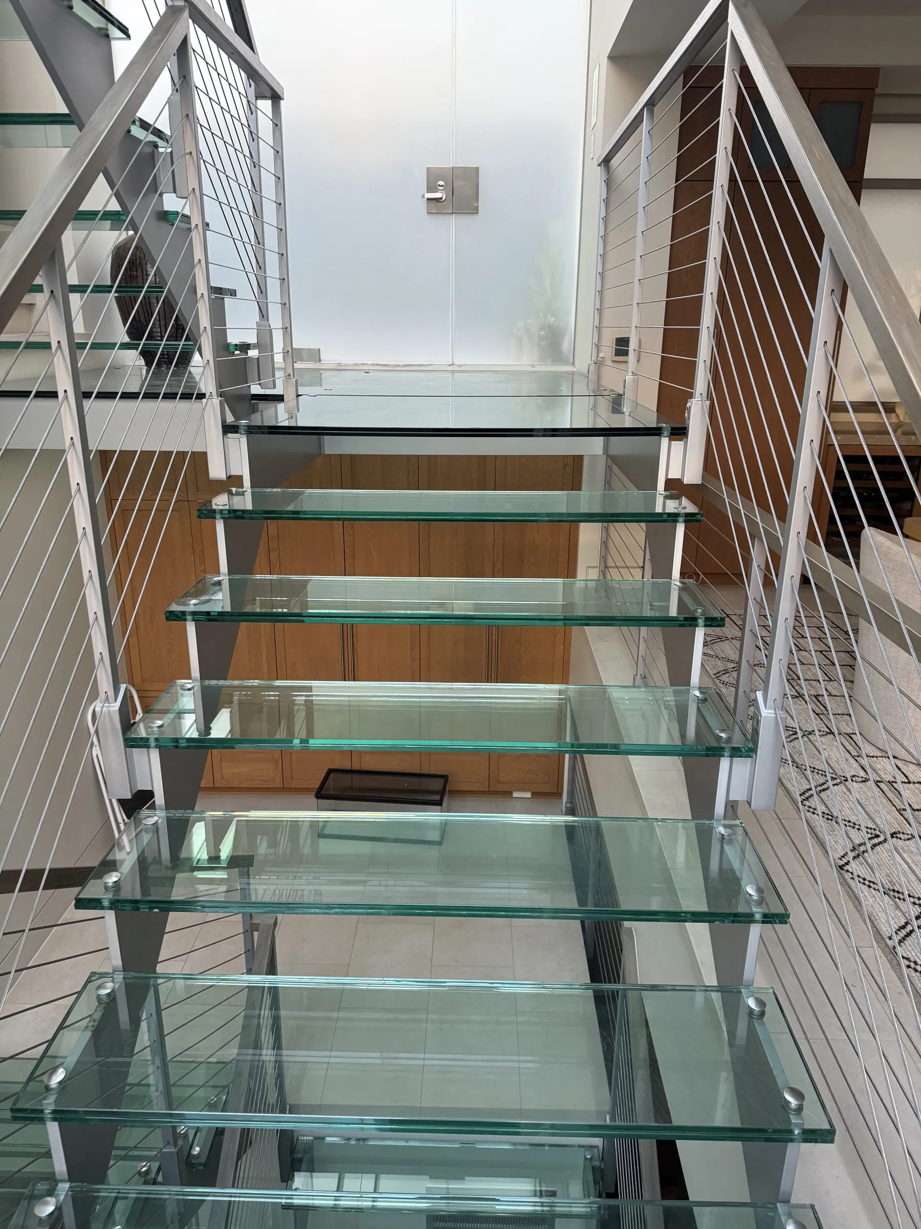 Open staircase with thick glass treads between steel stringers and cable railings