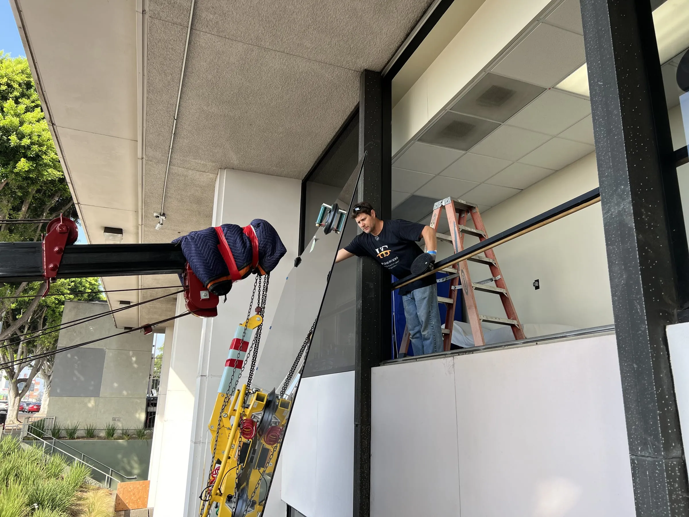HG Glass & Doors installer in a company shirt guiding a large glass panel on a vacuum lifter into a window opening