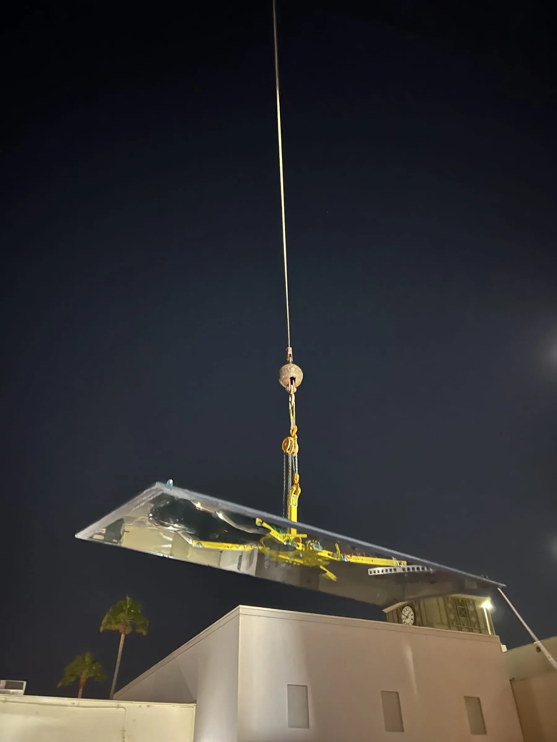 Large glass panel hanging from a crane at night above a building