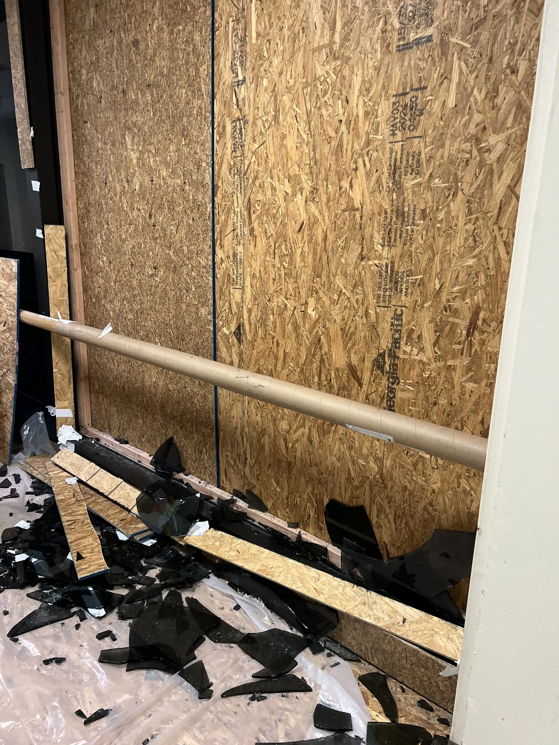 Broken storefront opening boarded up with plywood at night, with broken glass on the floor