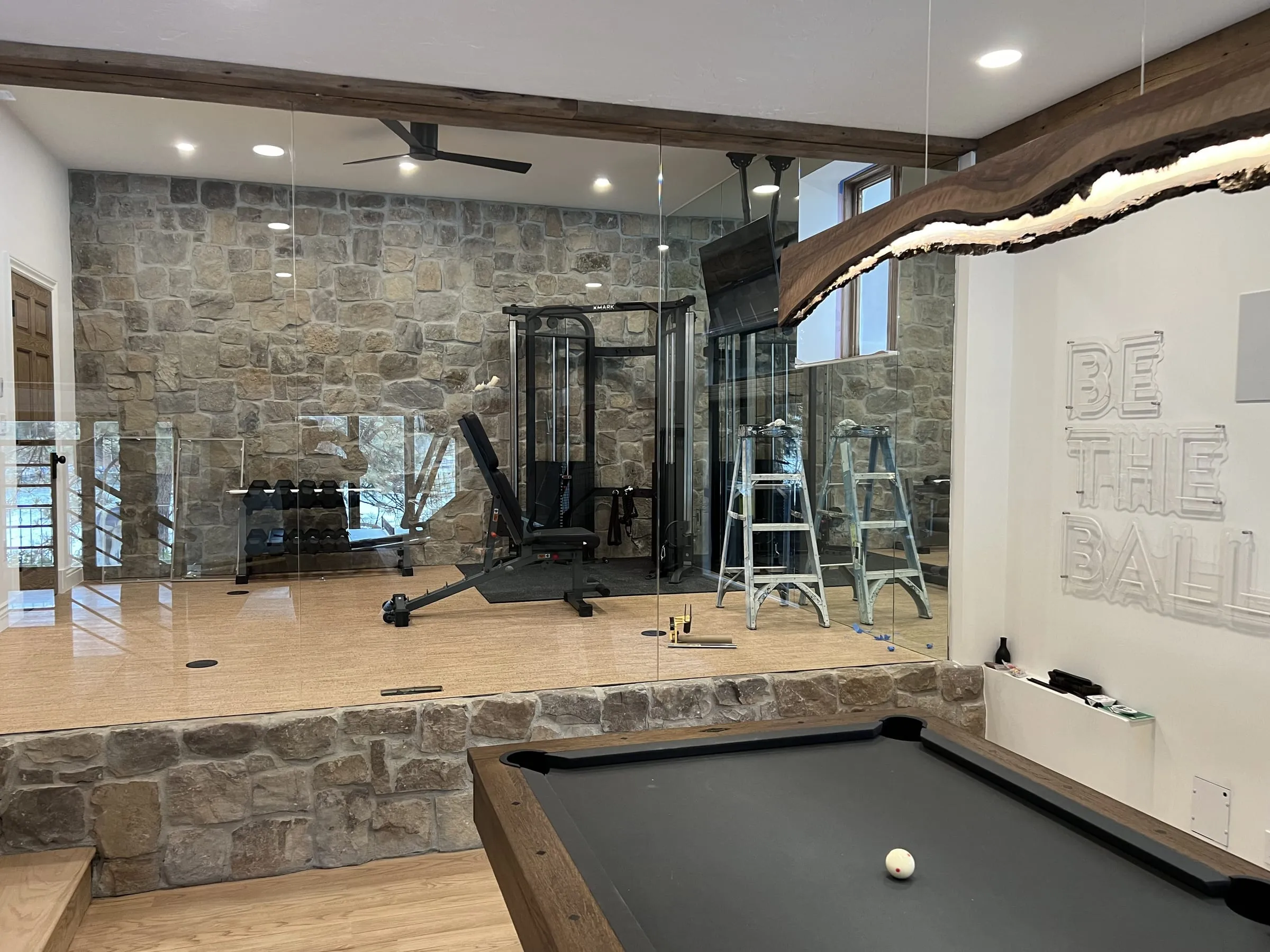 Raised home gym enclosed by frameless glass on a stone knee wall