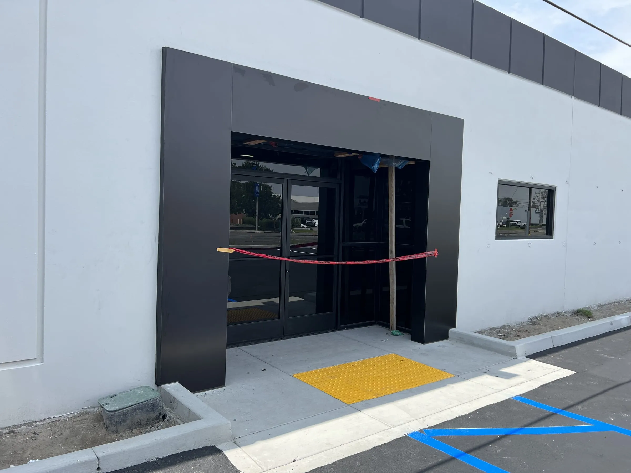 Commercial storefront entrance with black-framed glass doors, transom and sidelights inside a dark metal portal