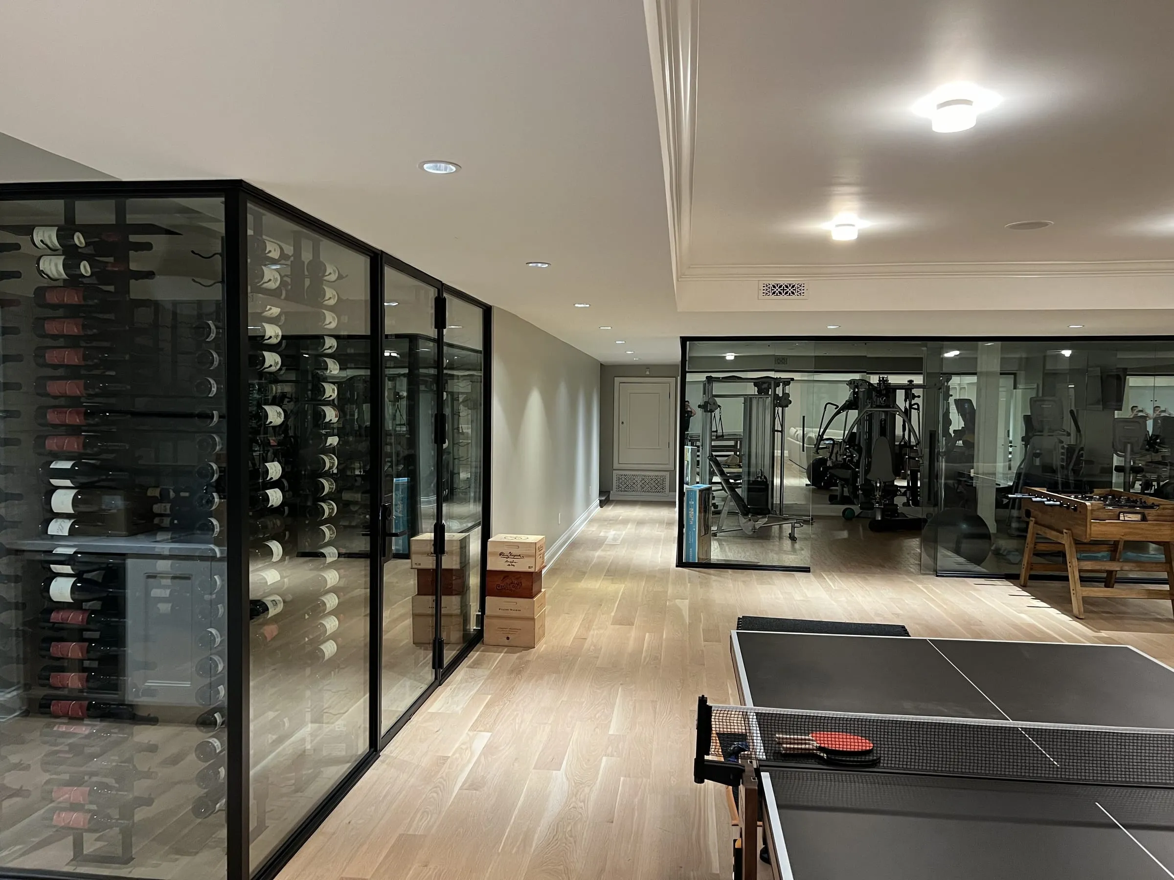 Glass wine room and glass gym enclosure seen across a games room